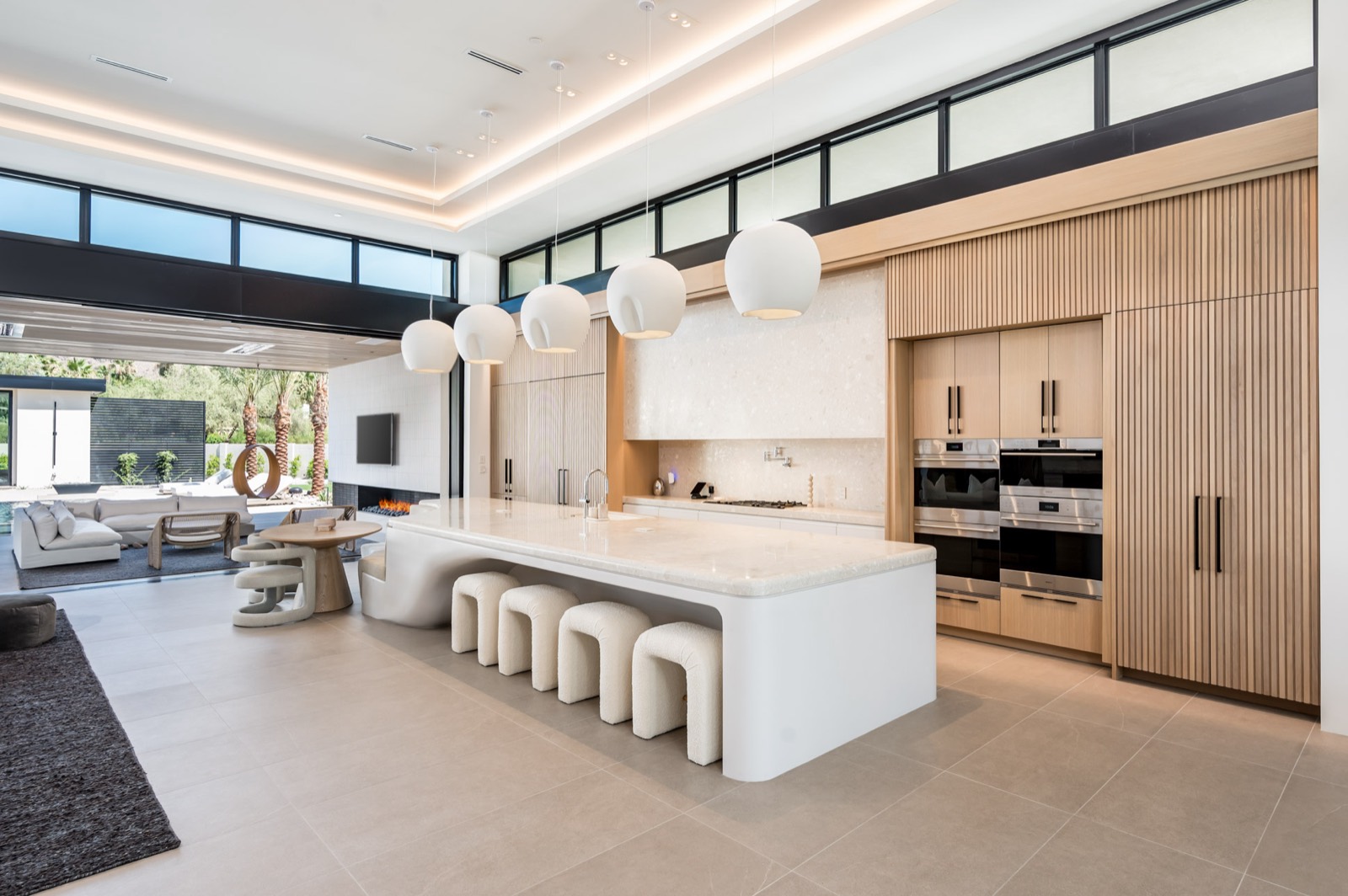 Open kitchen with a curved white island, pale oak cabinetry wall and clerestory windows