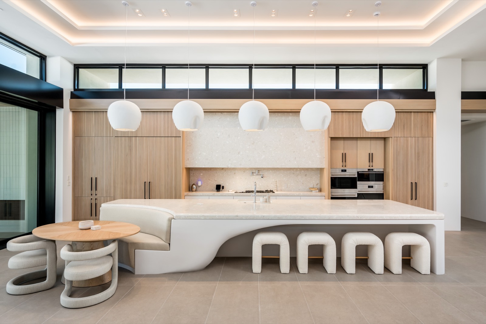 Sculptural white island with round stools in front of a full-height oak cabinetry wall