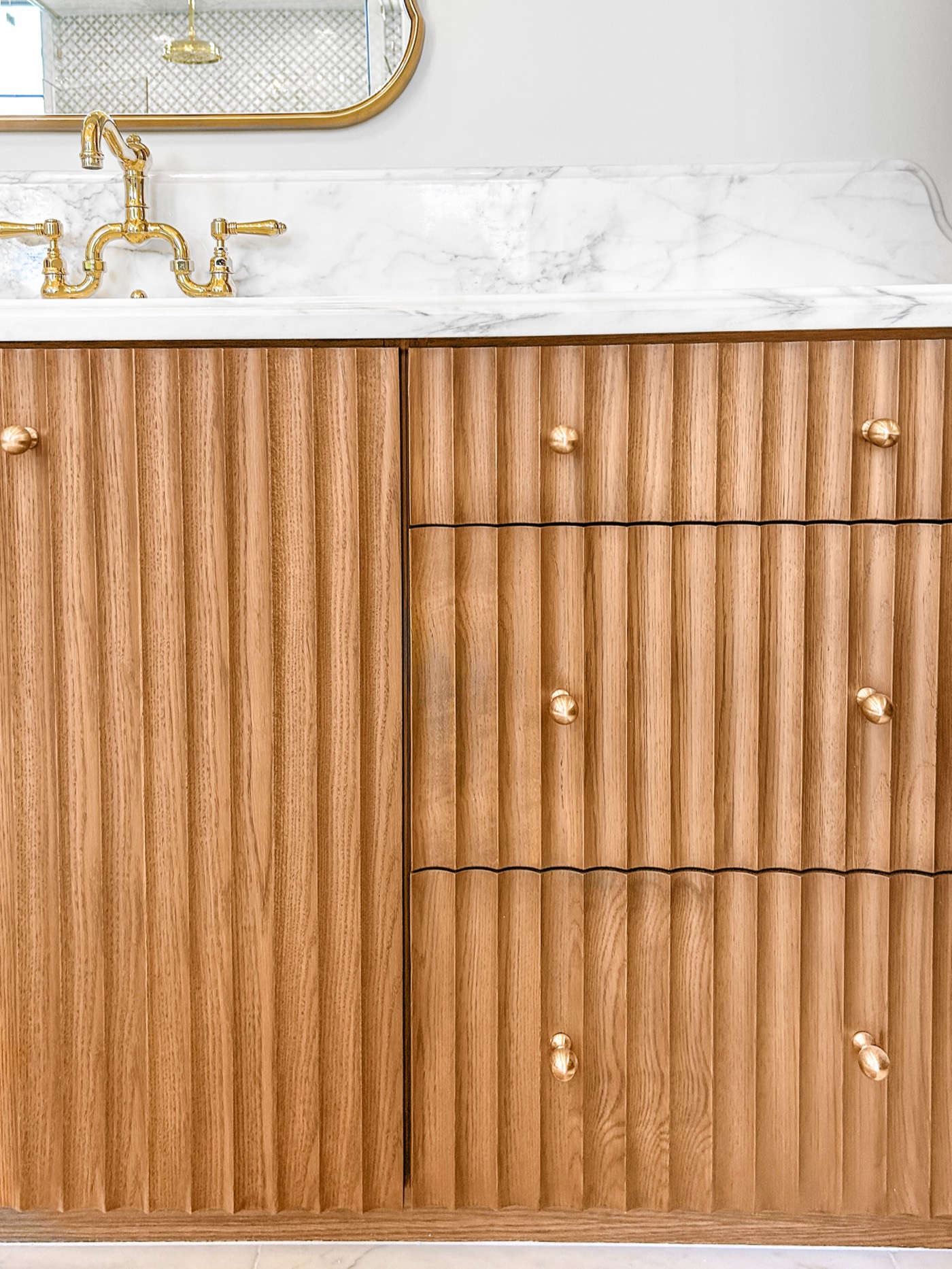 Fluted wood drawer fronts with slim brass pulls beneath a marble top