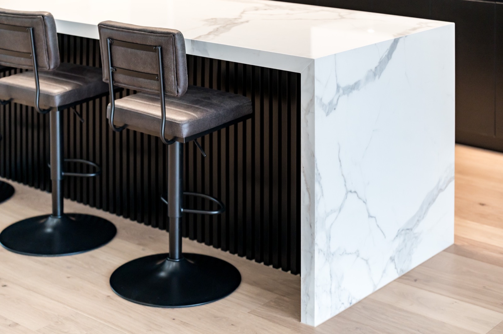 Waterfall island end beside black bar stools