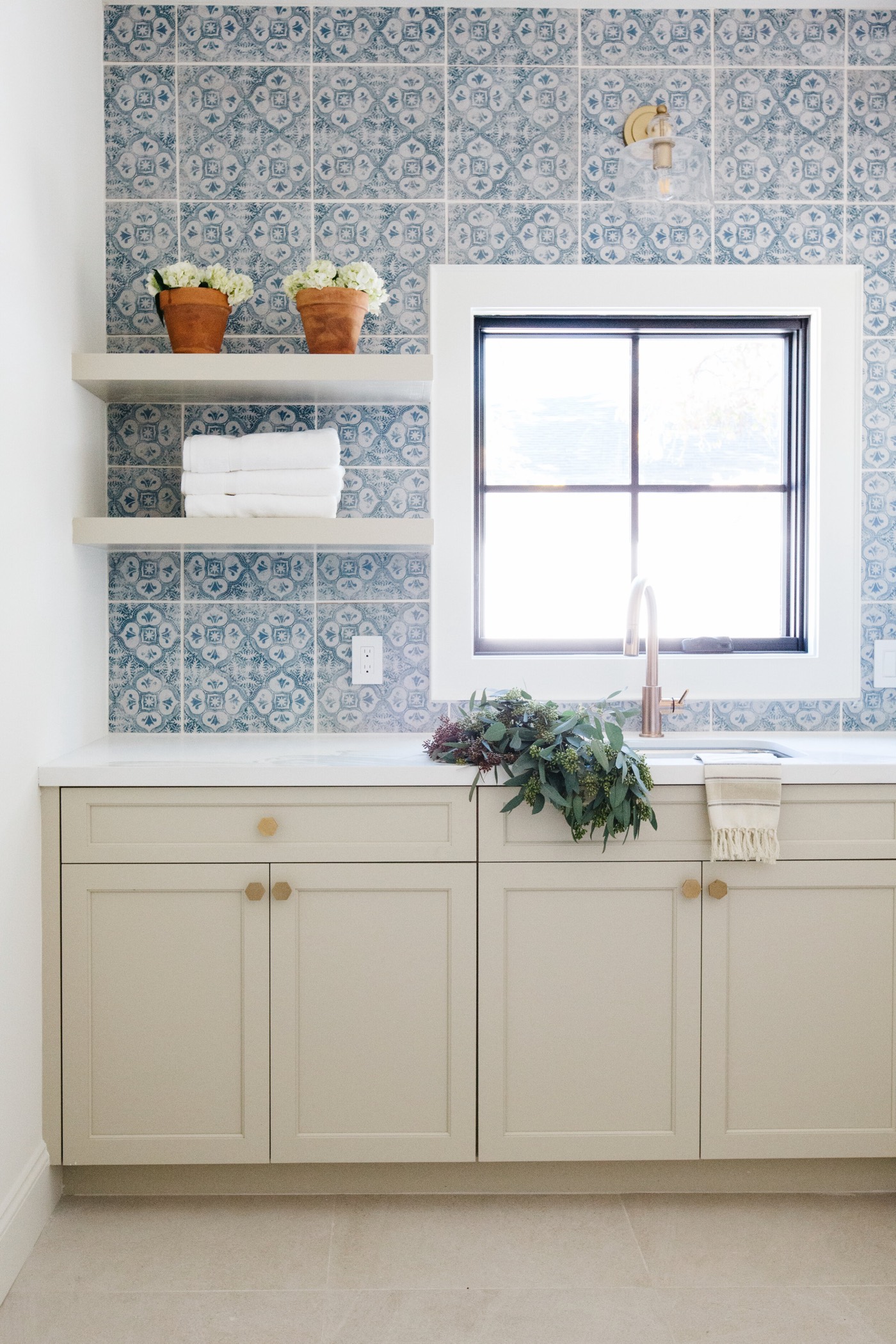 Painted cabinetry and open shelves beneath a window framed in blue patterned tile