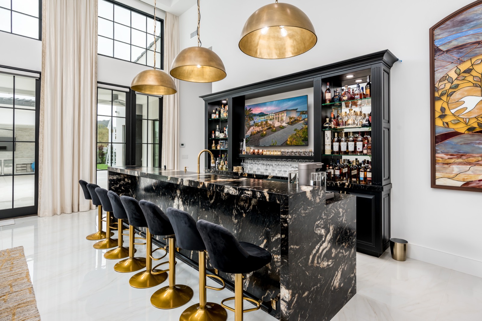Bar seating beneath brass pendants in front of lit shelving