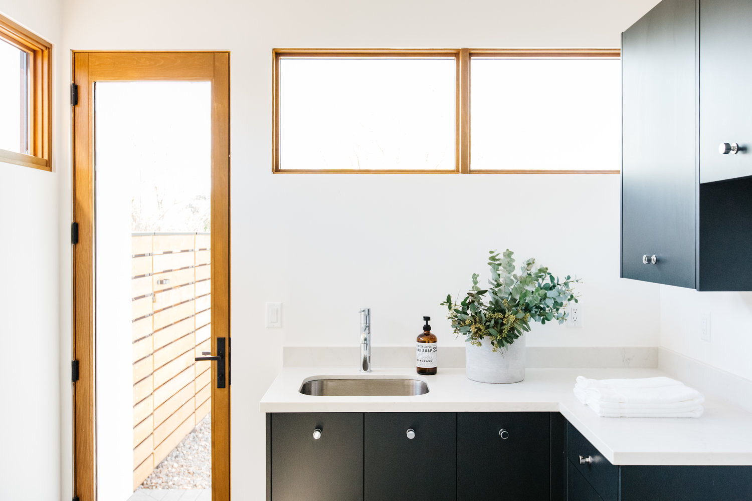 Black kitchen cabinetry beneath a window and an oak door