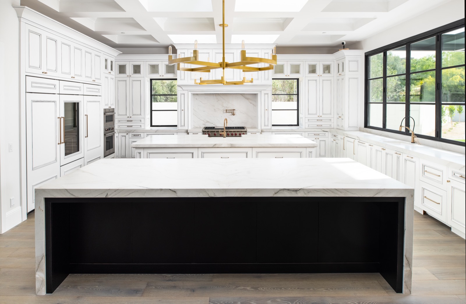 White kitchen with a black island and brass chandeliers