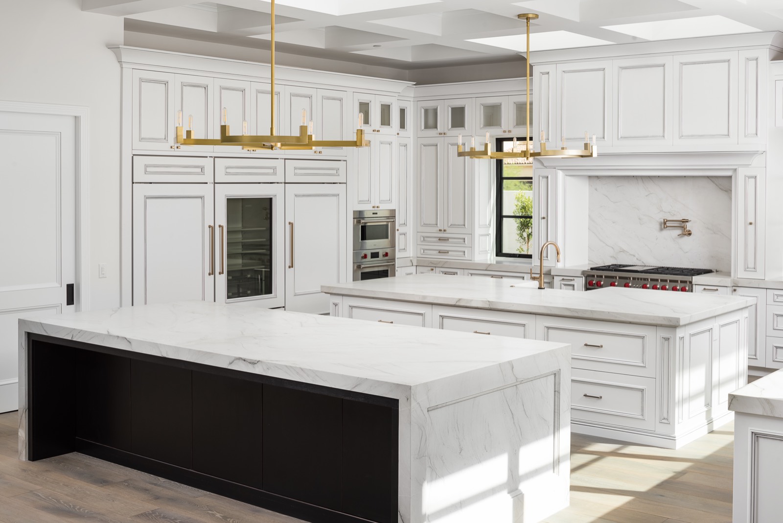 Black island with a marble top in a white coffered kitchen